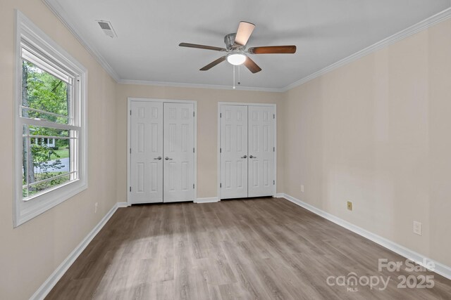 unfurnished bedroom featuring baseboards, wood finished floors, two closets, and multiple windows