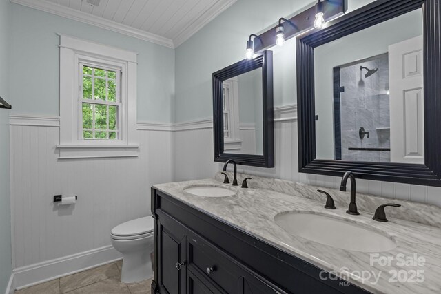 bathroom with a tile shower, double vanity, toilet, and a sink