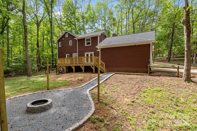 back of property with a fire pit, a shingled roof, fence, and a deck