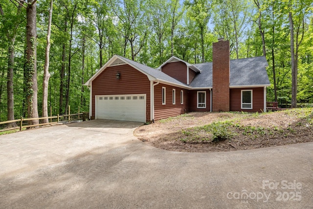 view of front facade with a chimney, fence, a shingled roof, driveway, and a garage