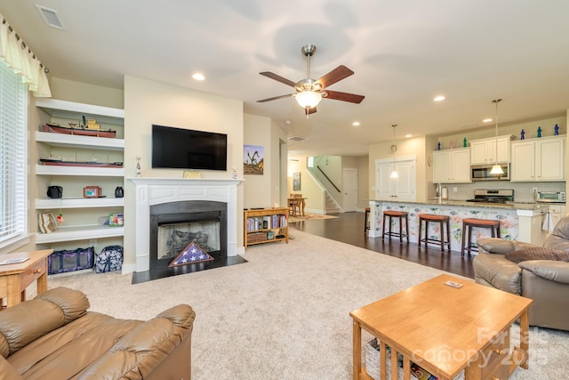 living area with stairway, a fireplace with flush hearth, a ceiling fan, light colored carpet, and recessed lighting