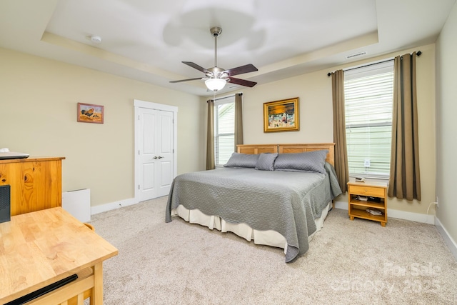 bedroom with baseboards, light colored carpet, a tray ceiling, and a ceiling fan