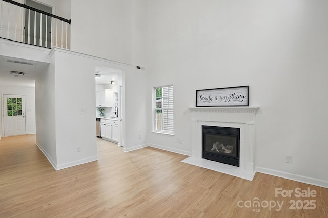 unfurnished living room with visible vents, a wealth of natural light, light wood-style floors, and a fireplace with flush hearth