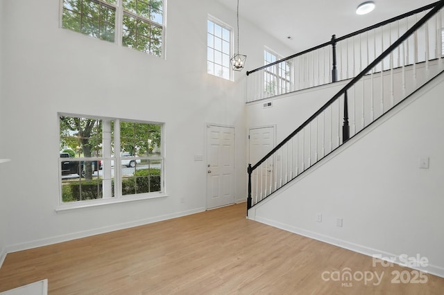 unfurnished living room featuring a towering ceiling, stairway, wood finished floors, and baseboards