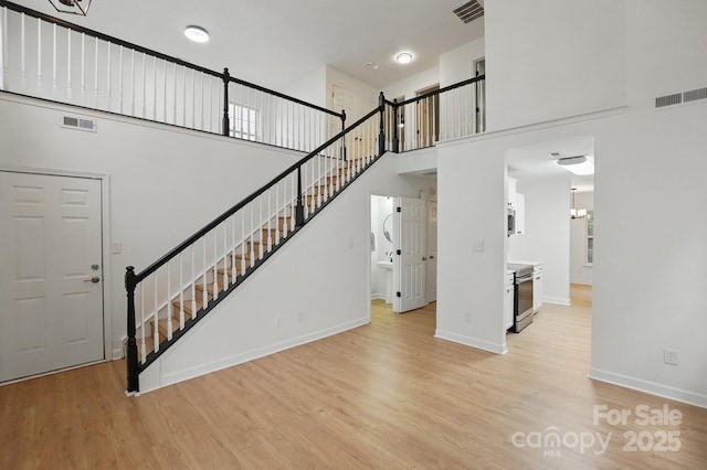 unfurnished living room featuring stairway, visible vents, and light wood-style flooring
