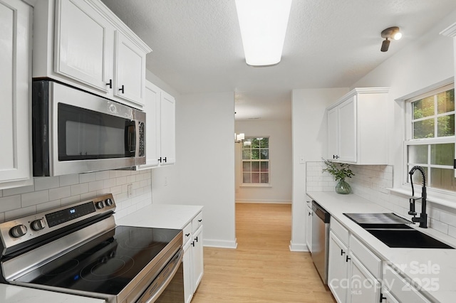 kitchen featuring light wood finished floors, a sink, a healthy amount of sunlight, white cabinets, and appliances with stainless steel finishes