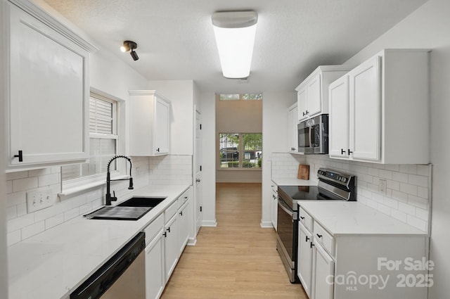 kitchen with light wood finished floors, a sink, white cabinets, and appliances with stainless steel finishes