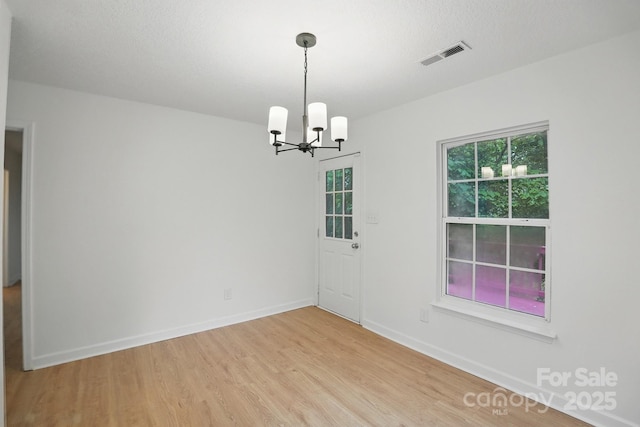 unfurnished dining area featuring baseboards, visible vents, an inviting chandelier, and light wood-style floors