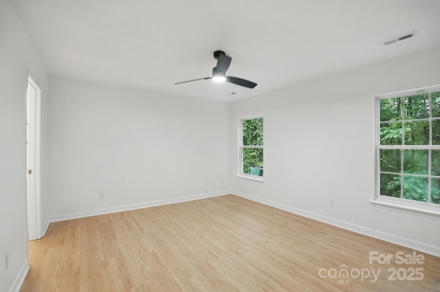empty room featuring light wood finished floors, ceiling fan, a wealth of natural light, and visible vents