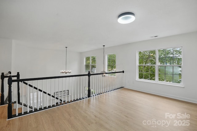 hallway with baseboards, visible vents, wood finished floors, and an inviting chandelier