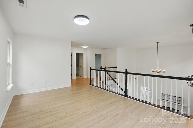 spare room with baseboards, visible vents, wood finished floors, and a notable chandelier