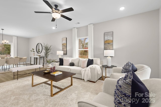 living room featuring a healthy amount of sunlight, wood finished floors, visible vents, and ceiling fan with notable chandelier