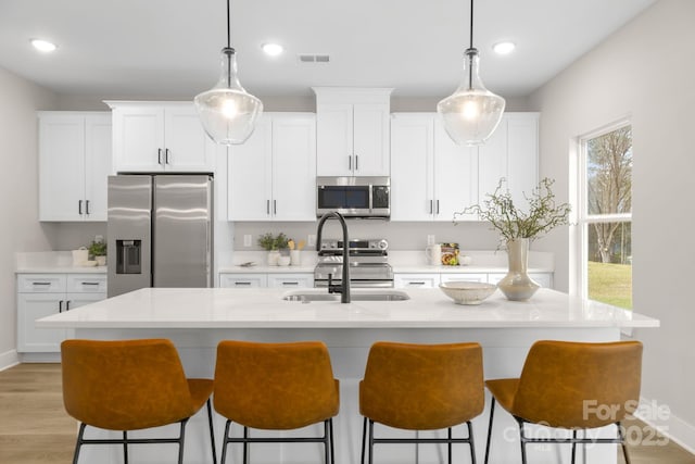 kitchen featuring a kitchen breakfast bar, a sink, stainless steel appliances, white cabinetry, and visible vents