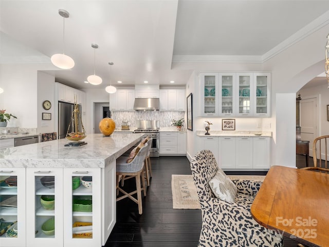 kitchen with arched walkways, stainless steel appliances, white cabinets, under cabinet range hood, and a kitchen island