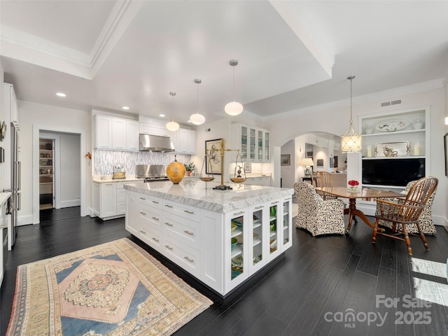 kitchen featuring under cabinet range hood, glass insert cabinets, arched walkways, ornamental molding, and visible vents
