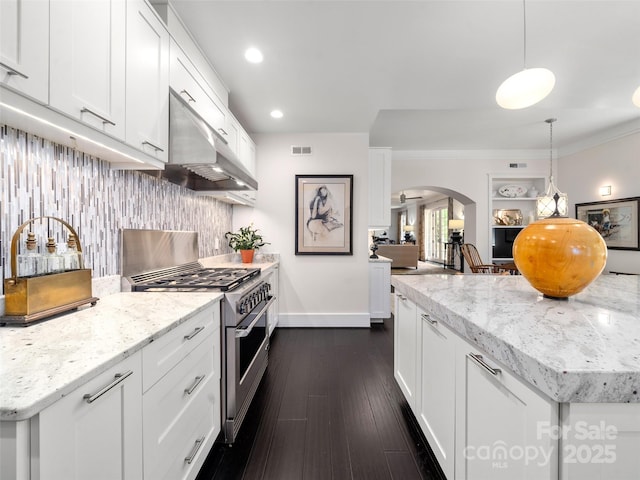 kitchen featuring under cabinet range hood, high end stainless steel range, arched walkways, baseboards, and tasteful backsplash