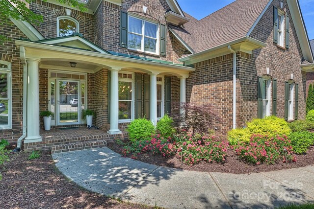 entrance to property with roof with shingles, brick siding, and covered porch