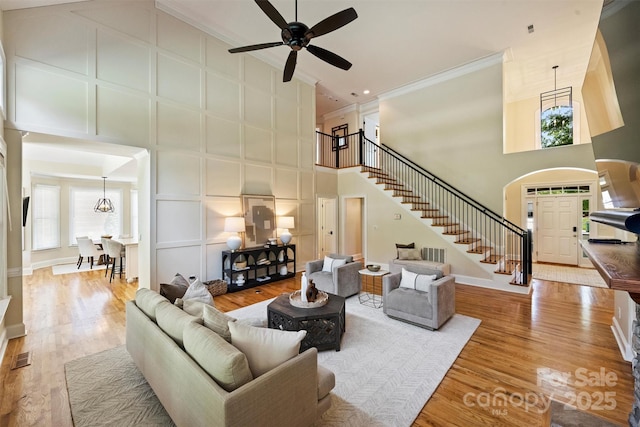 living room featuring wood finished floors, stairway, a towering ceiling, ceiling fan, and ornamental molding