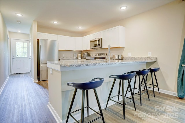 kitchen with a kitchen breakfast bar, white cabinetry, a peninsula, stainless steel appliances, and light wood-style flooring