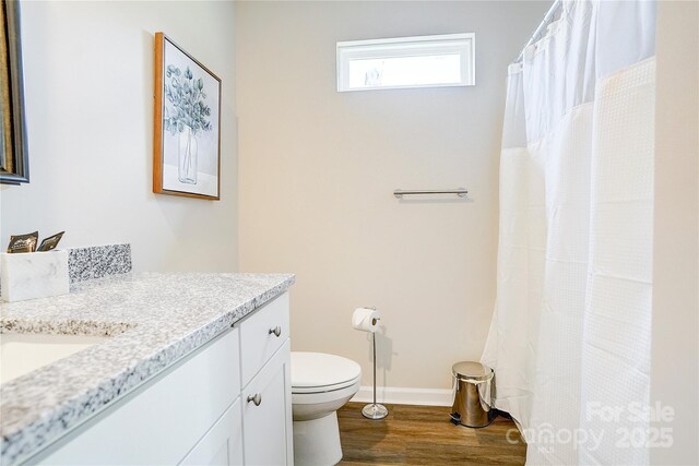 bathroom featuring vanity, baseboards, wood finished floors, and toilet