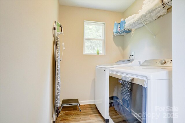 clothes washing area with laundry area, baseboards, wood finished floors, and washer and dryer