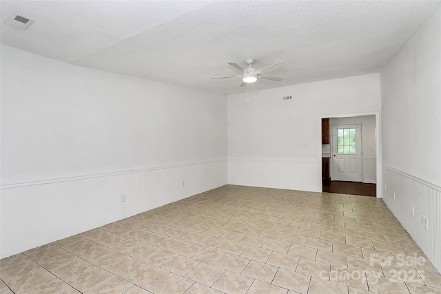 tiled spare room featuring a ceiling fan, visible vents, and a wainscoted wall