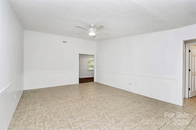 empty room featuring a textured ceiling, visible vents, wainscoting, and ceiling fan