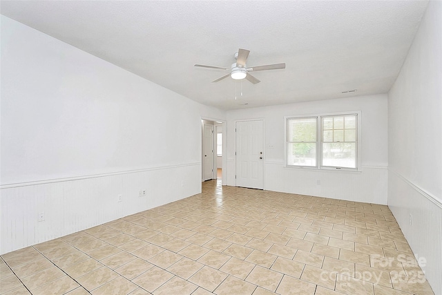 empty room with ceiling fan and a wainscoted wall