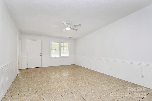 spare room with ceiling fan and a wainscoted wall