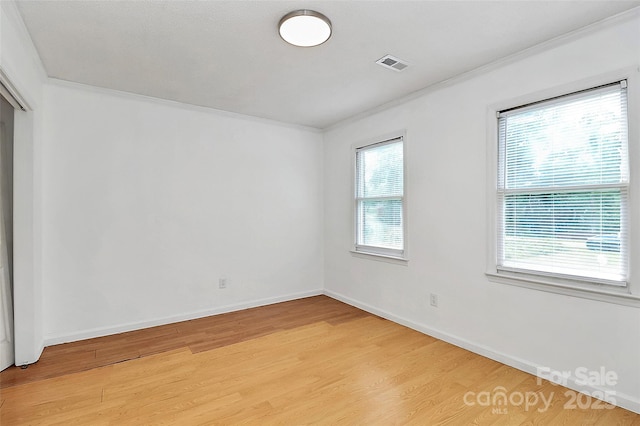 unfurnished room with visible vents, light wood-style flooring, baseboards, and ornamental molding