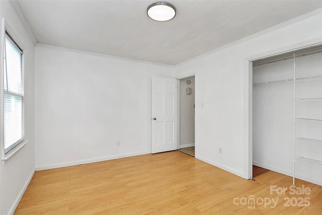 unfurnished bedroom with baseboards, crown molding, light wood finished floors, and a closet