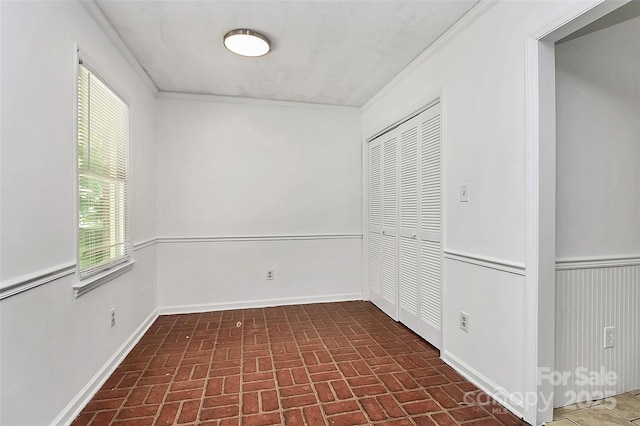 interior space featuring a closet, brick floor, baseboards, and crown molding