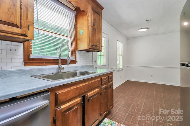 kitchen with brick patterned floor, dishwasher, baseboards, a sink, and tasteful backsplash