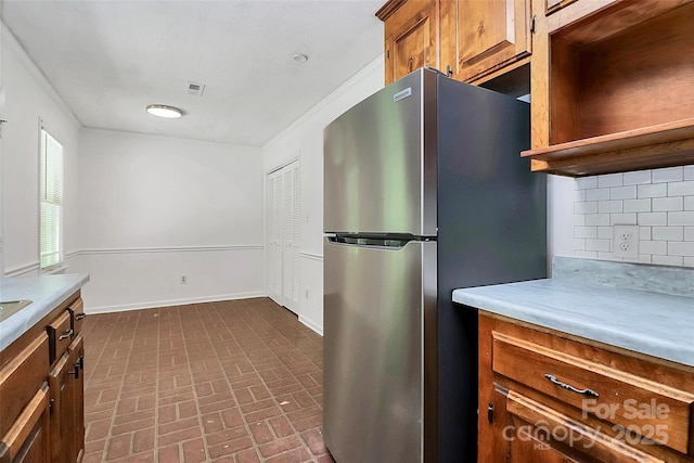kitchen with freestanding refrigerator, light countertops, brick patterned floor, and backsplash