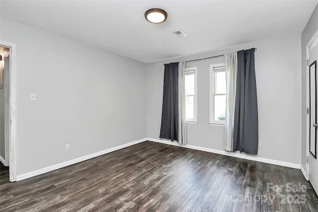 unfurnished room featuring baseboards, visible vents, and dark wood finished floors