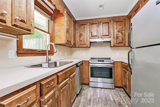 kitchen with a sink, brown cabinetry, under cabinet range hood, and appliances with stainless steel finishes