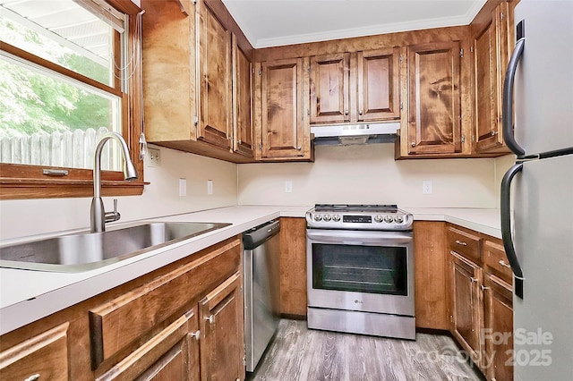 kitchen featuring under cabinet range hood, appliances with stainless steel finishes, brown cabinetry, and a sink