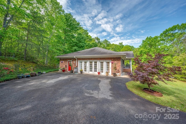 view of front of house with brick siding, driveway, french doors, and roof with shingles