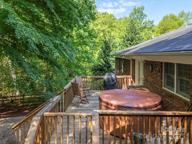 deck featuring a covered hot tub, area for grilling, and a forest view