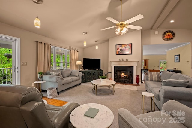 carpeted living room featuring lofted ceiling with beams, ceiling fan, and a warm lit fireplace