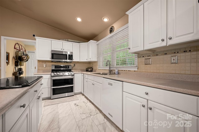 kitchen with decorative backsplash, vaulted ceiling, a sink, stainless steel appliances, and white cabinetry
