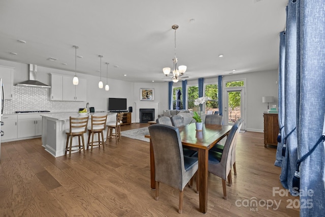 dining space featuring an inviting chandelier, a fireplace, recessed lighting, and wood finished floors
