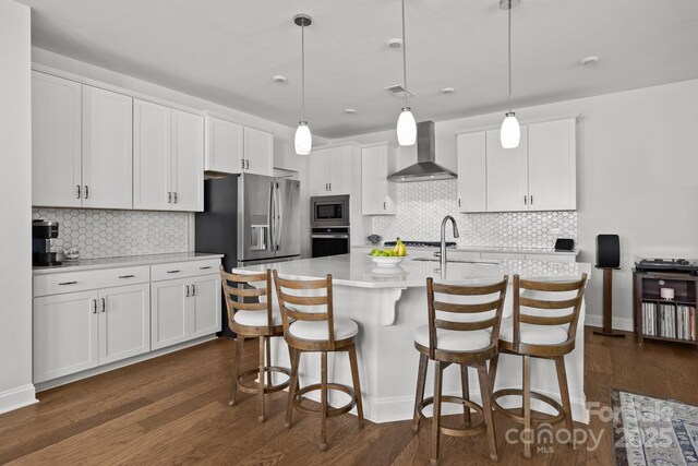 kitchen with decorative backsplash, wall chimney range hood, light countertops, white cabinets, and appliances with stainless steel finishes