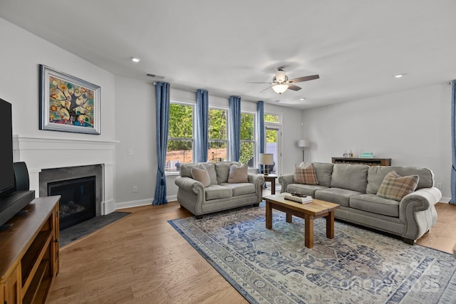 living room featuring a ceiling fan, a fireplace with flush hearth, wood finished floors, baseboards, and recessed lighting