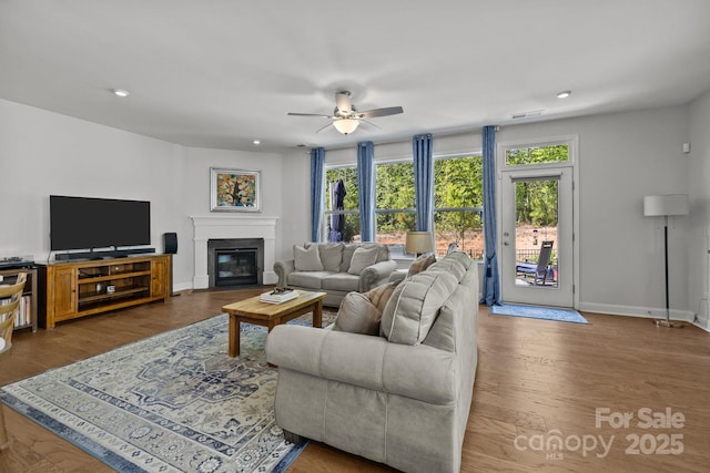 living room with baseboards, a ceiling fan, a glass covered fireplace, and a healthy amount of sunlight
