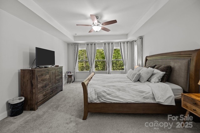 bedroom with light colored carpet, a ceiling fan, baseboards, and a tray ceiling