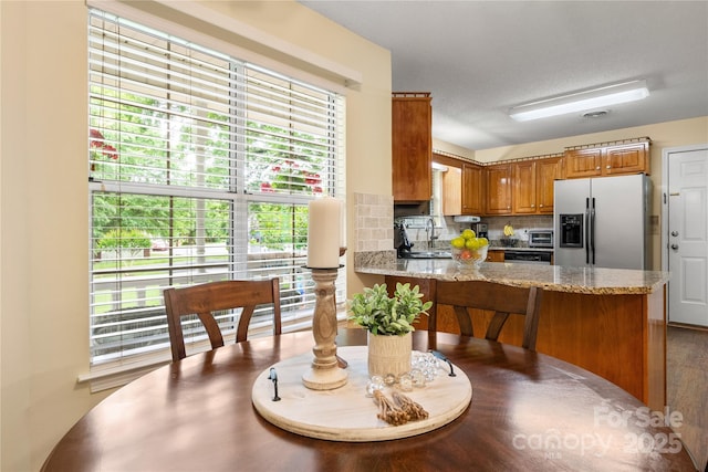 kitchen with stainless steel fridge, brown cabinetry, plenty of natural light, a peninsula, and backsplash
