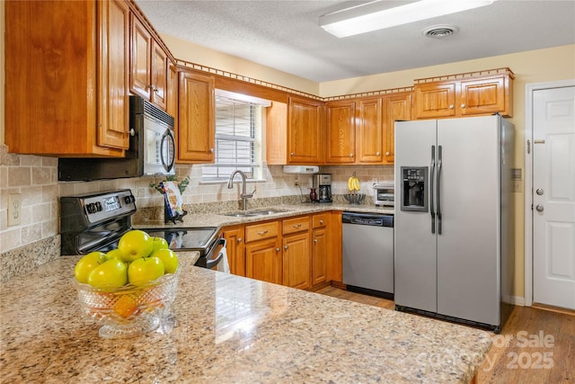 kitchen featuring brown cabinets, light stone counters, appliances with stainless steel finishes, a sink, and light wood-style floors