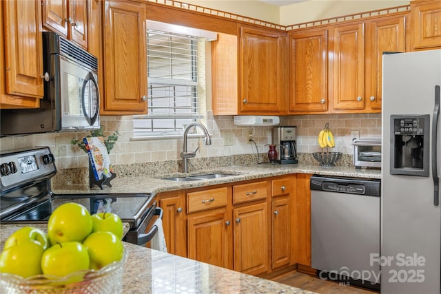 kitchen with appliances with stainless steel finishes, tasteful backsplash, brown cabinets, a sink, and light stone counters
