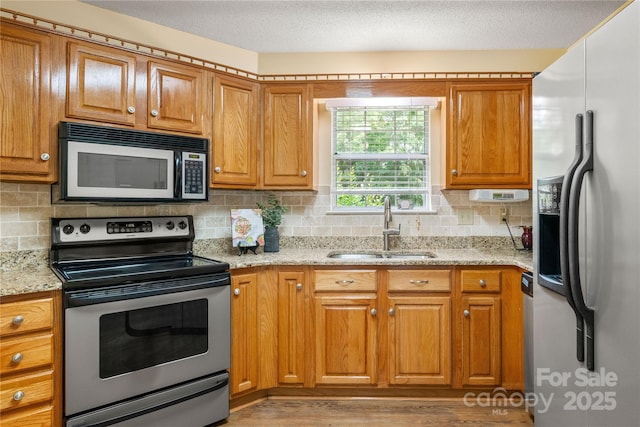 kitchen featuring brown cabinetry, tasteful backsplash, stainless steel range with electric cooktop, a sink, and refrigerator with ice dispenser